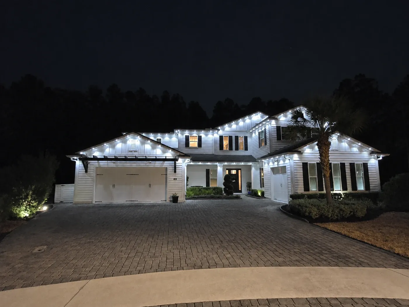 Two-story home with bright white lighting tracing its layered rooflines, gables and front entry at night.